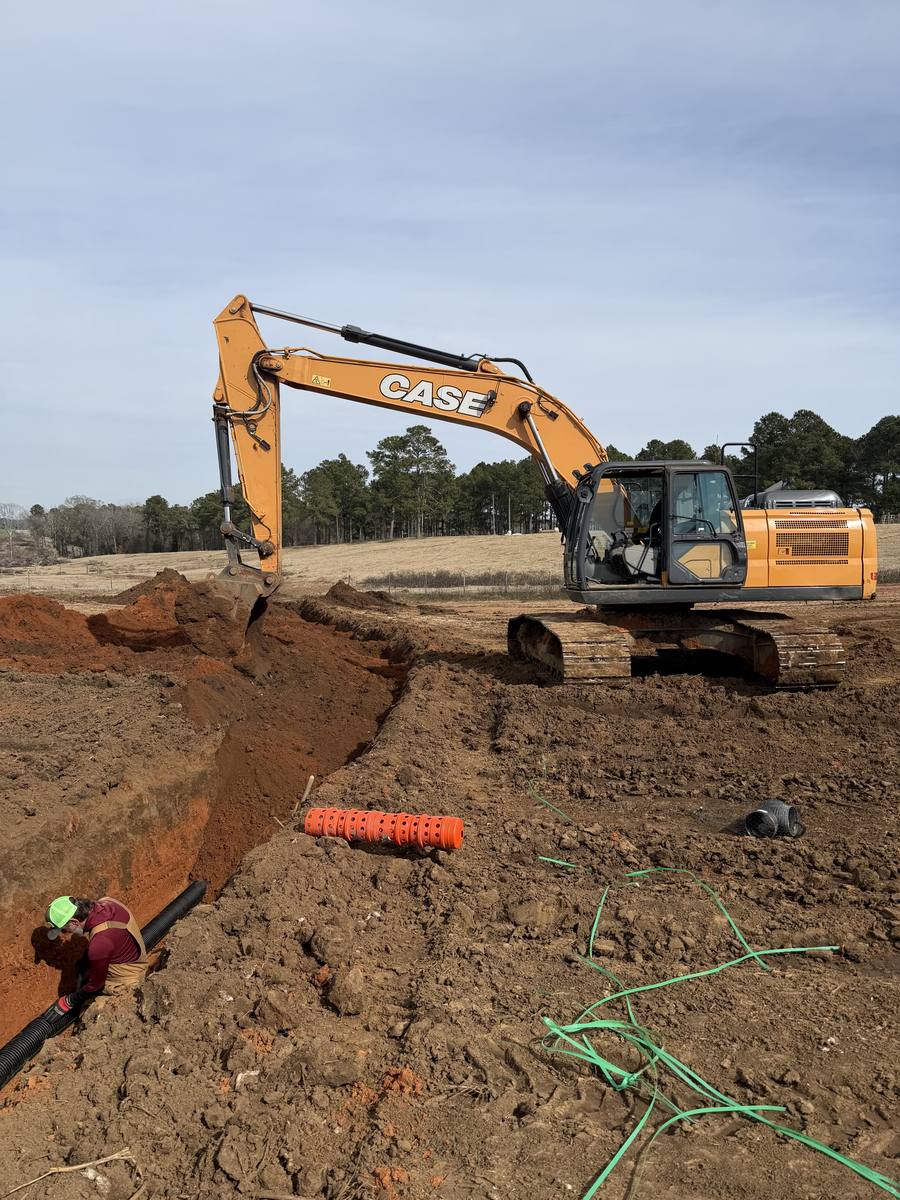 Excavator digging a utility trench while pipe goes in